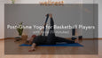 A person practices a leg stretch on a blue yoga mat in a cozy, well-lit room decorated with plants and warm lights.